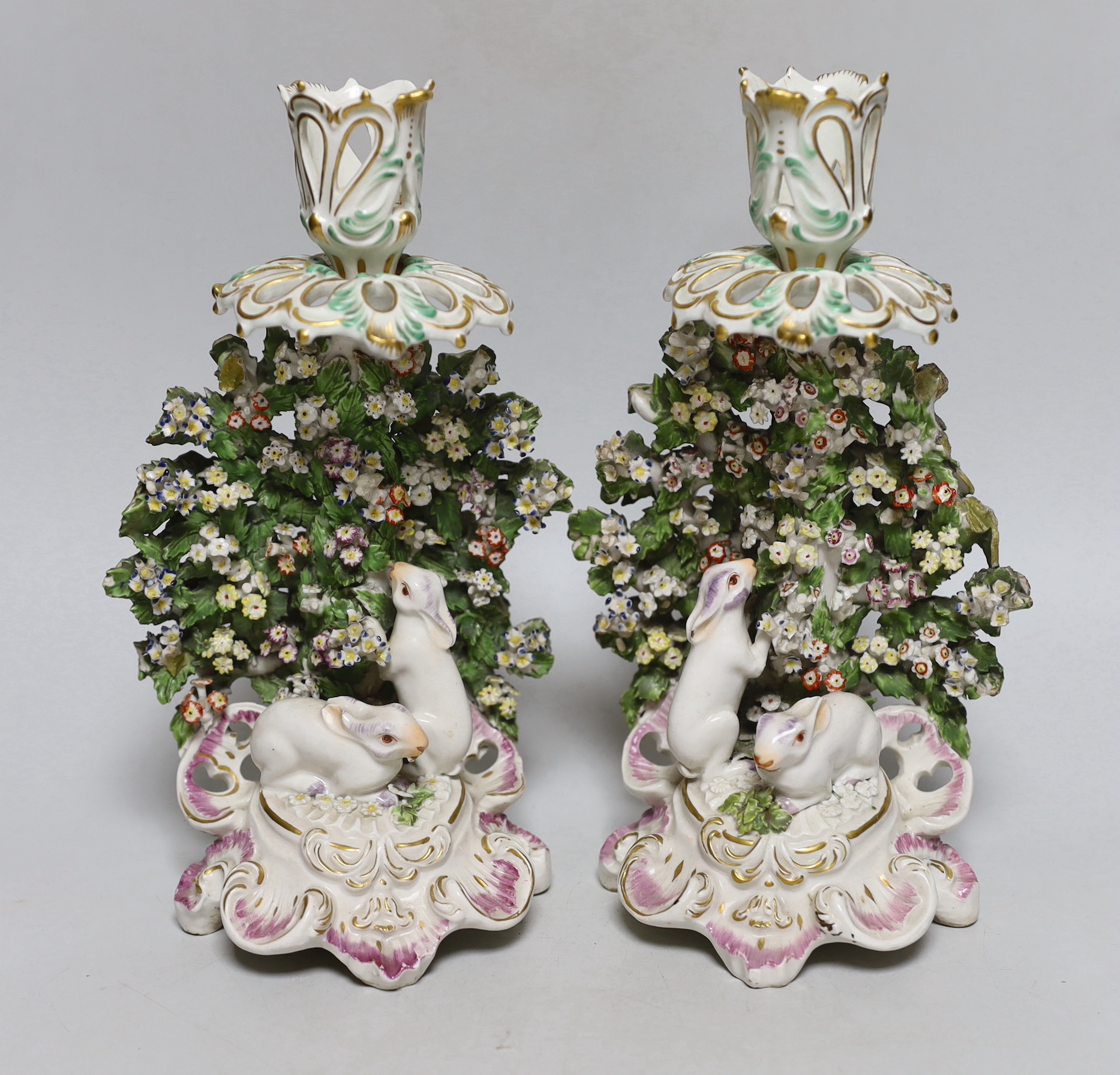 A good pair of Derby candlestick figures of rabbits before a brocage, the elaborate sconce highlighted in green and gold, 23cm high